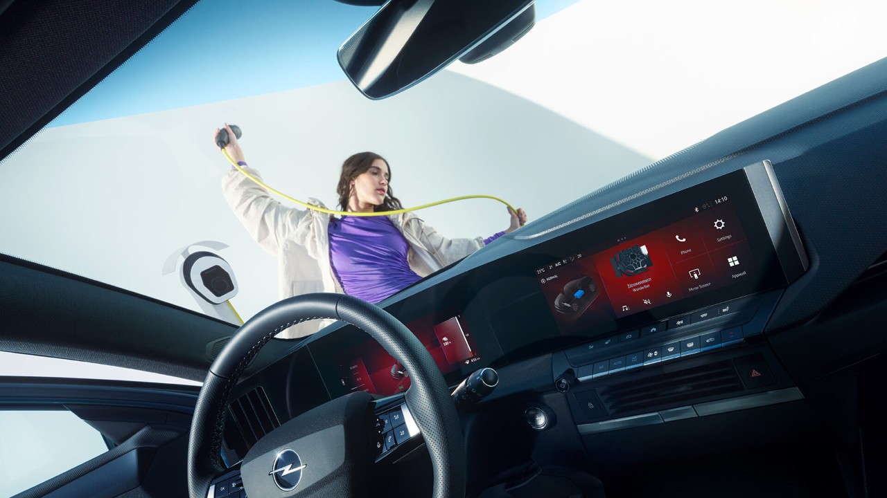 Primer plano del interior de un Opel Astra Sports Tourer Electric con una mujer sosteniendo el cable de carga del vehículo eléctrico en el exterior.