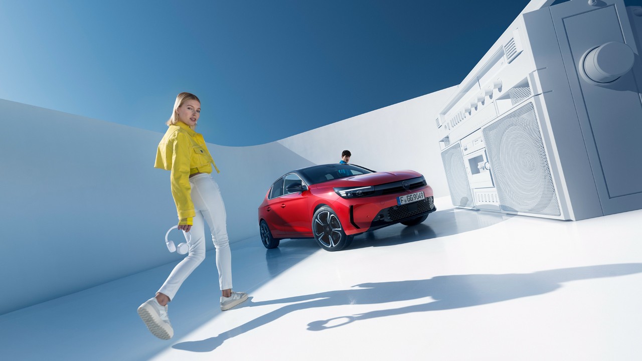 Mujer junto al nuevo Opel Corsa de color rojo con techo negro y un hombre entrando por la puerta del conductor