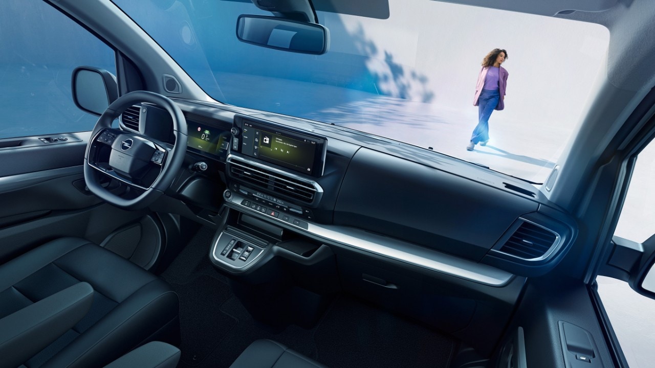 Vista interior de un Opel Zafira blanco desde el asiento del acompañante con una mujer de pie en el exterior